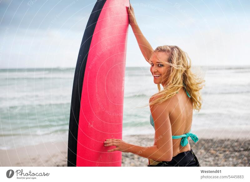 Lächelnde Frau am Strand mit Surfbrett Beach Straende Strände Beaches Surfbretter surfboard surfboards Surfen Surfing Wellenreiten weiblich Frauen Wassersport