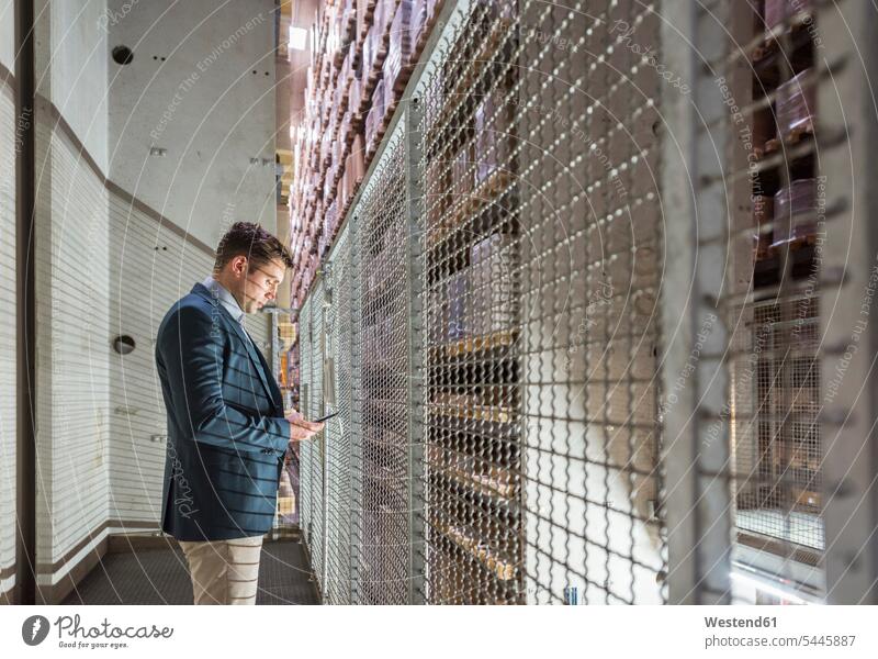 Mann im automatisierten Hochregallager schaut auf Handy Männer männlich arbeiten Arbeit Mobiltelefon Handies Handys Mobiltelefone Erwachsener erwachsen Mensch