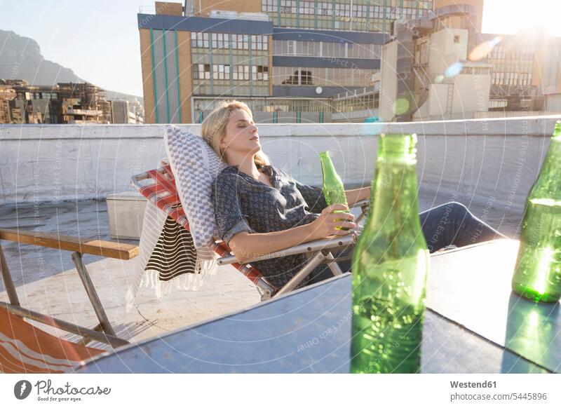 Junge Frau entspannt sich auf ihrer Terrasse weiblich Frauen genießen geniessen Genuss blond blonde Haare blondes Haar Dachterrasse Dachterrassen Bier Auszeit