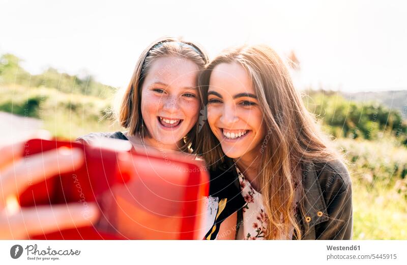Zwei glückliche Mädchen machen ein Selfie im Freien Schwester Schwestern weiblich lachen Portrait Porträts Portraits Glück glücklich sein glücklichsein Selfies