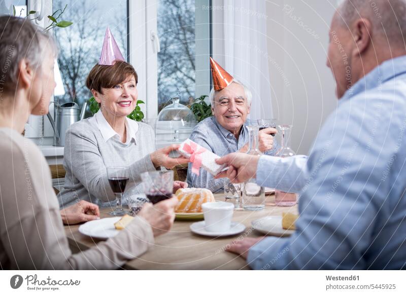Zwei ältere Paare feiern Geburtstag und stoßen mit Rotwein an anstoßen zuprosten anstossen Rotweine trinken Geburtstagsfeiern Geburtstage Partyhut Papphut