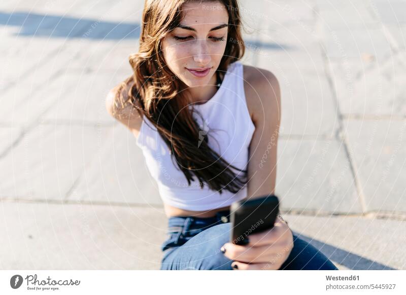Junge Frau entspannt sich an der Strandpromenade und schaut auf ihr Handy weiblich Frauen Smartphone iPhone Smartphones Erwachsener erwachsen Mensch Menschen