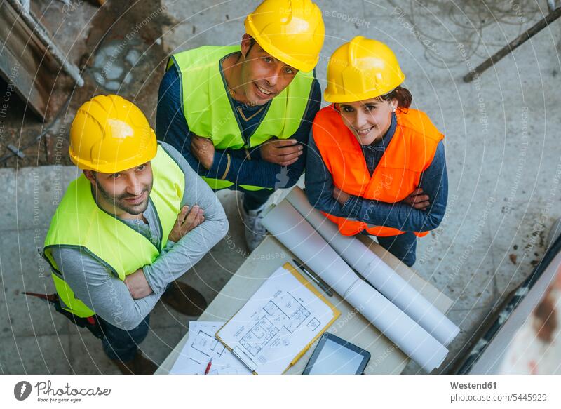 Porträt einer lächelnden Frau und zweier Männer in Arbeitskleidung mit Bauplan Architekturplan Bauzeichnung Bauarbeiter Kollegen Arbeitskollegen Baustelle