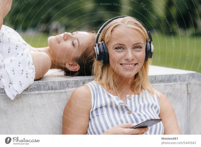 Porträt einer jungen Frau mit Handy und Kopfhörer in einem Skatepark Mobiltelefon Handies Handys Mobiltelefone Kopfhoerer weiblich Frauen lächeln Skateboardpark