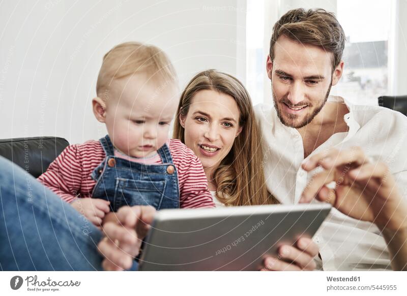 Eltern mit kleinem Mädchen schauen Tablette auf Couch an glücklich Glück glücklich sein glücklichsein Familie Familien lächeln Tablet Computer Tablet-PC