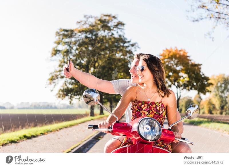 Glückliches junges Paar macht ein Selfie auf einem Motorroller auf einer Landstraße Selfies Roller Piaggio Landstraßen Pärchen Paare Partnerschaft glücklich