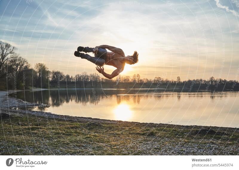 Deutschland, Bayern, Feldkirchen, Mann beim Parkour am Seeufer Seen springen hüpfen Parcour Männer männlich Gewässer Wasser Sprung Spruenge Sprünge Erwachsener