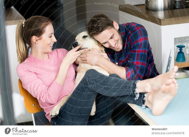 Glückliches junges Paar kuschelt zu Hause mit Hund Hunde glücklich glücklich sein glücklichsein kuscheln schmusen knuddeln Pärchen Paare Partnerschaft Zuhause