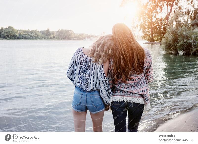 Rückenansicht von zwei Teenager-Mädchen beim Sonnenuntergang am Flussufer Freundinnen Teenagerin junges Mädchen Teenagerinnen weiblich junge Frau Strand Beach
