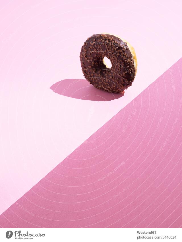 Doughnut mit Schokoladenglasur auf rosa Grund Food and Drink Lebensmittel Essen und Trinken Nahrungsmittel pink pinkfarben rosa Hintergrund Schatten Nahaufnahme