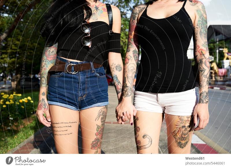 Tätowiertes lesbisches Paar, das im Sommer auf der Straße Händchen hält Tattoo Tätowierungen Tatoos Taetowierung Tattoos Taetowierungen Frau weiblich Frauen