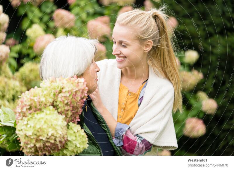 Glückliche junge Frau mit ihrer Großmutter am Busch im Garten Gärten Gaerten Gartenanlage Gartenanlagen Grossmutter Oma Grossmama Großmütter Omi glücklich
