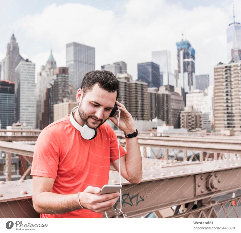 USA, New York City, Sportler auf der Brooklyn Brige mit Handy und Kopfhörern Kopfhoerer Mann Männer männlich Brücke Bruecken Brücken Mobiltelefon Handies Handys