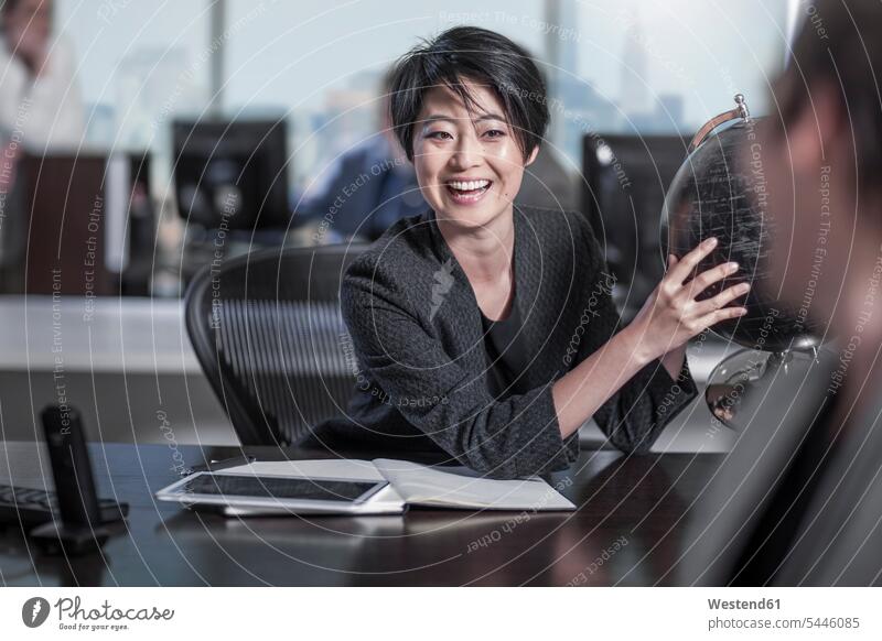 Lachende Frau mit Globus sitzt am Schreibtisch im Stadtbüro Kollegen Arbeitskollegen Büro Office Büros lachen sprechen reden Weltkugel Erdkugel Globen