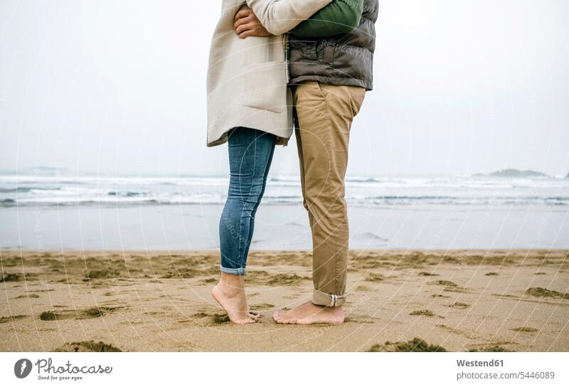 Niedriger Teil eines barfüssig am Strand stehenden Paares steht Beach Straende Strände Beaches Pärchen Partnerschaft Mensch Menschen Leute People Personen Bein