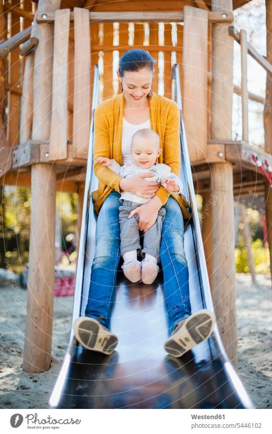 Glückliches kleines Mädchen sitzt mit seiner Mutter auf dem Spielplatz auf einer Rutsche Baby Babies Babys Säuglinge Kind Kinder Rutschen sitzen sitzend