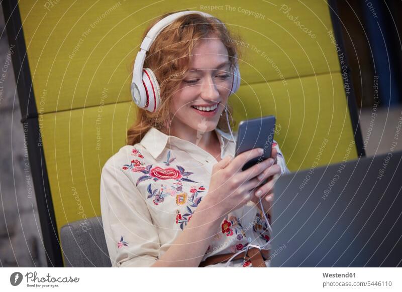 Junge Frau, die in einem modernen Kreativbüro arbeitet, Kopfhörer trägt und ein Smartphone benutzt Büro Office Büros arbeiten Arbeit telefonieren anrufen Anruf