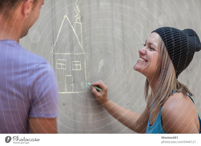 Mann und Frau zeichnen ein Haus mit Kreide auf Betonwand Männer männlich weiblich Frauen Betonwände Betonwaende Zeichnung Häuser Haeuser Wand Wände Waende