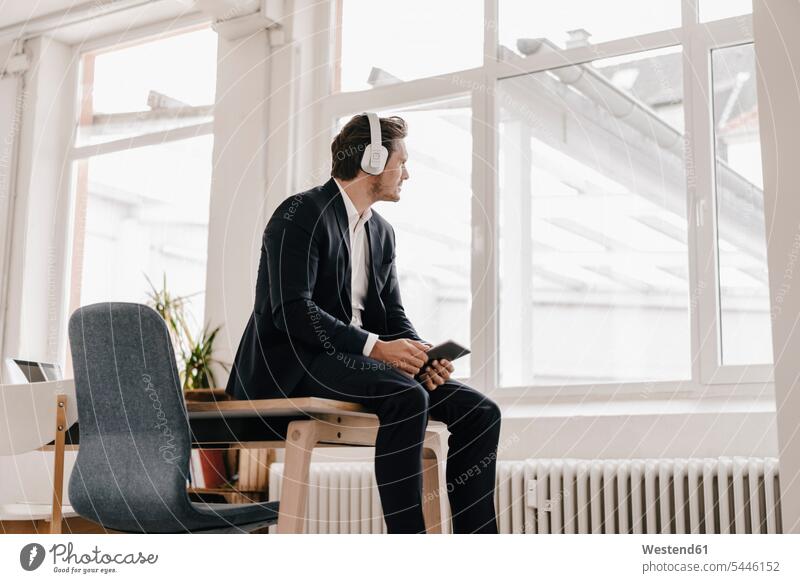 Geschäftsmann mit Tablett und Kopfhörer auf dem Tisch sitzend Kopfhoerer entspannt entspanntheit relaxt sitzt hören hoeren Mann Männer männlich Tablet Computer