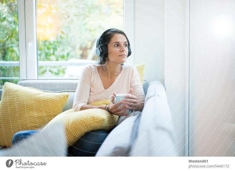Frau sitzt allein auf dem Sofa und hört Musik mit Kopfhörern Musik hören sitzen sitzend Kopfhoerer Allein alleine einzeln Couches Liege Sofas Kaffee