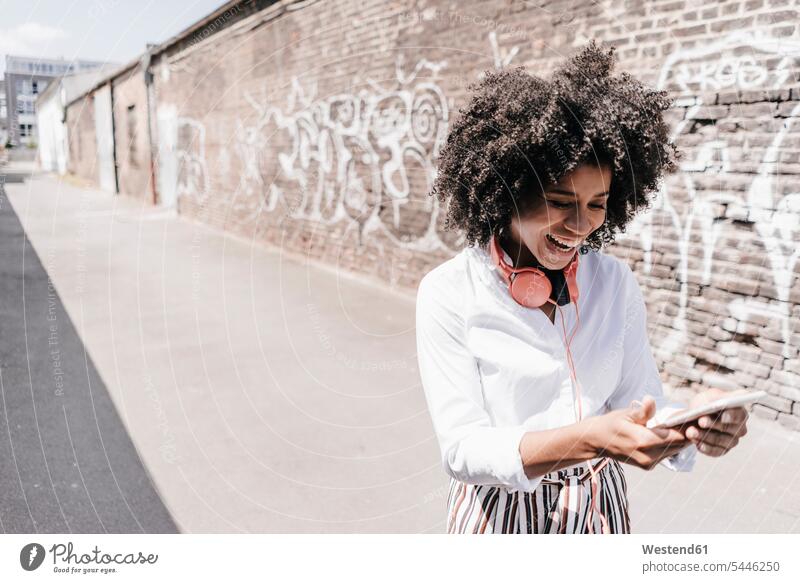 Glückliche junge Frau, die draußen auf ihr Handy schaut lachen Mobiltelefon Handies Handys Mobiltelefone stehen stehend steht weiblich Frauen positiv Emotion