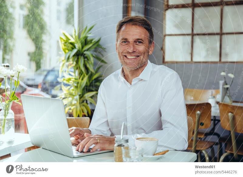 Porträt eines lächelnden Geschäftsmannes, der in einem Café mit Laptop arbeitet Notebook Laptops Notebooks Businessmann Businessmänner Geschäftsmänner arbeiten