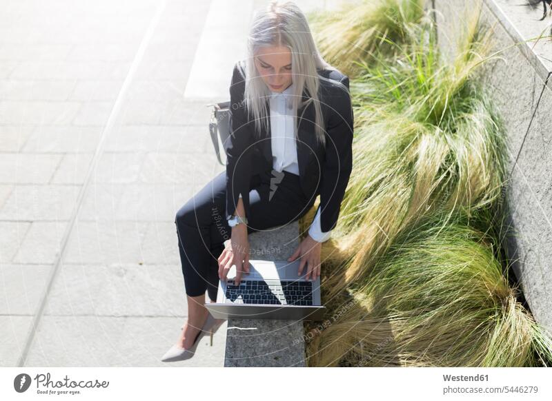 Junge Geschäftsfrau, die in der Stadt mit einem Laptop an einer Wand sitzt Geschäftsfrauen Businesswomen Businessfrauen Businesswoman Frau weiblich Frauen