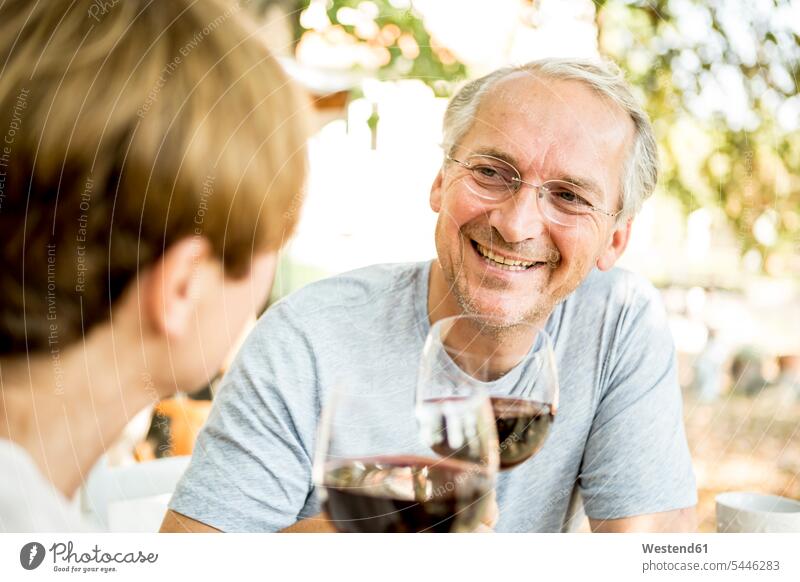 Lächelndes älteres Paar, das im Freien Rotweingläser klimpert Pärchen Paare Partnerschaft Wein Weine lächeln Mensch Menschen Leute People Personen Alkohol