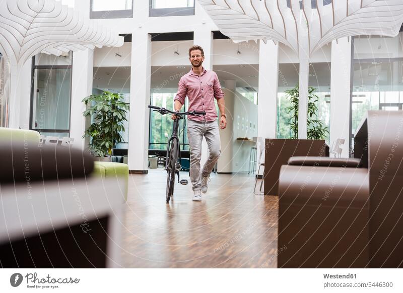 Mann mit Fahrrad zu Fuß im Büro Bikes Fahrräder Räder Rad gehen gehend geht lächeln Männer männlich Raeder Erwachsener erwachsen Mensch Menschen Leute People