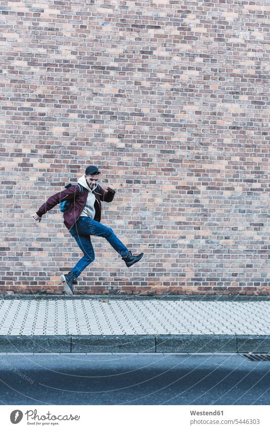 Junger Mann springt vor Ziegelmauer Männer männlich springen hüpfen Erwachsener erwachsen Mensch Menschen Leute People Personen Sprung Spruenge Sprünge Gehsteig