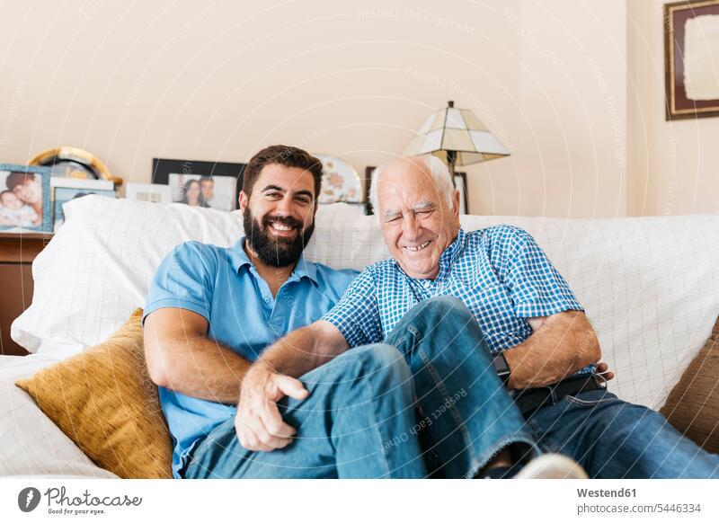 Porträt eines erwachsenen Enkels und seines Großvaters, die zu Hause auf der Couch sitzen und sich gegenseitig kitzeln Enkelsöhne Enkelsohn Opa Großpapa