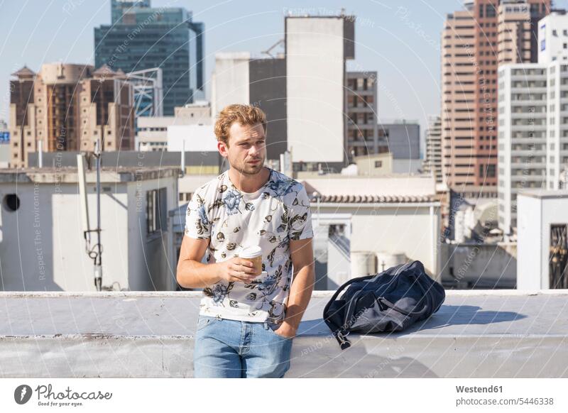 Junger Mann steht auf der Dachterrasse und trinkt Kaffee Männer männlich genießen geniessen Genuss blond blonde Haare blondes Haar Dachterrassen trinken