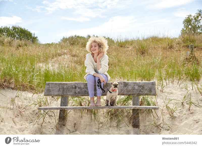Porträt einer glücklichen jungen Frau, die mit ihrem Hund auf einer Bank in den Dünen sitzt weiblich Frauen Hunde Erwachsener erwachsen Mensch Menschen Leute