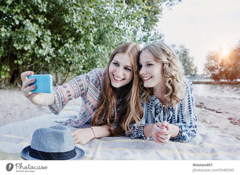 Zwei Teenager-Mädchen liegen auf einer Decke am Strand und machen ein Selfie Freundinnen Selfies Freunde Freundschaft Kameradschaft liegend liegt Smartphone