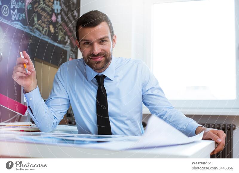 Porträt eines selbstbewussten Geschäftsmannes am Schreibtisch im Kreativbüro lächeln Businessmann Businessmänner Geschäftsmänner Portrait Porträts Portraits
