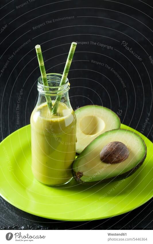 Glasflasche mit Avocado-Smoothie und geschnittener Avocado auf einem Teller Niemand Avocados Persea americana Hälfte halbe halbiert halber Haelfte
