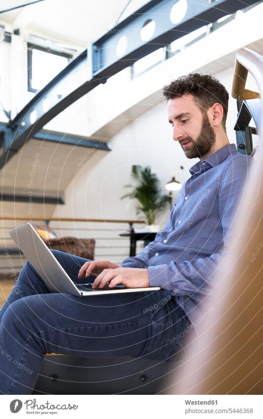 Mann sitzt in einem modernen Büro mit Laptop auf dem Boden Männer männlich Notebook Laptops Notebooks sitzen sitzend Office Büros Erwachsener erwachsen Mensch
