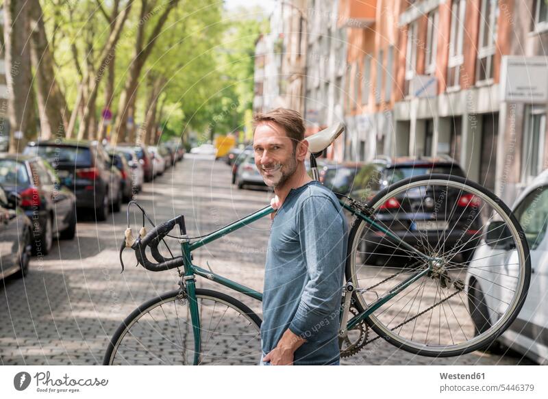 Porträt eines lächelnden reifen Mannes, der sein Fahrrad auf der Schulter trägt Portrait Porträts Portraits Bikes Fahrräder Räder Rad Männer männlich Raeder