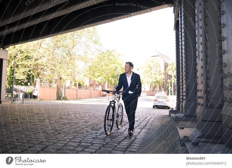 Älterer Geschäftsmann schiebt Fahrrad in der Stadt gehen gehend geht Businessmann Businessmänner Geschäftsmänner Bikes Fahrräder Räder Rad staedtisch städtisch