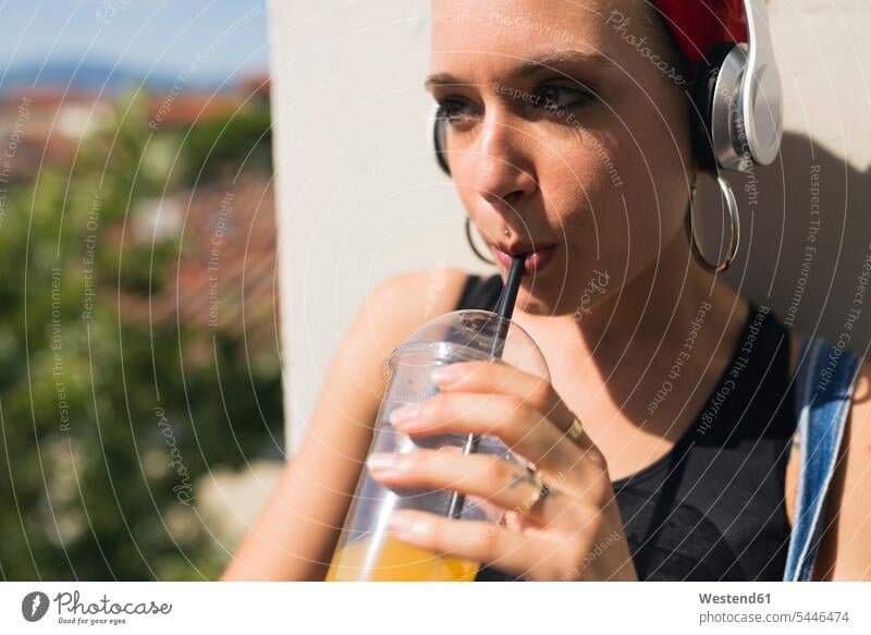 Porträt einer jungen Frau mit Kopfhörern, die ein Erfrischungsgetränk trinkt Kopfhoerer weiblich Frauen trinken Erwachsener erwachsen Mensch Menschen Leute