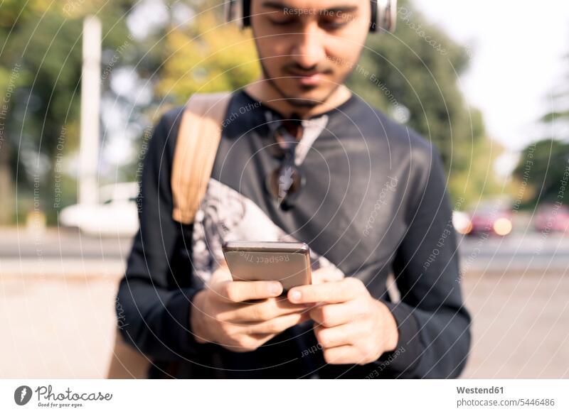 Junger Mann mit Kopfhörern und Handy im Freien Musik Männer männlich hören hoeren Mobiltelefon Handies Handys Mobiltelefone Kopfhoerer Erwachsener erwachsen