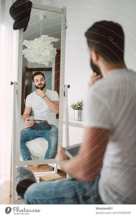 Junger Mann sitzt auf dem Bett und betrachtet sich im Spiegel Zuhause zu Hause daheim Betten ansehen Männer männlich schauen sehend Erwachsener erwachsen Mensch