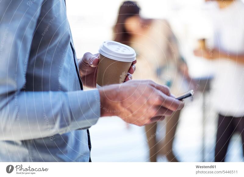 Hand eines Mannes, der eine Tasse Kaffee hält und ein Smartphone benutzt simsen Kommunikation Handy Mobiltelefon Handies Handys Mobiltelefone Erreichbarkeit
