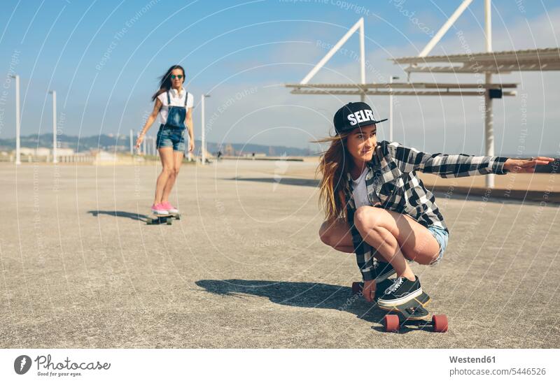Zwei junge Frauen beim Longboarding an der Strandpromenade weiblich Skateboarderin Skateboardfahrerin Skaterin Skateboarderinnen Skaterinnen