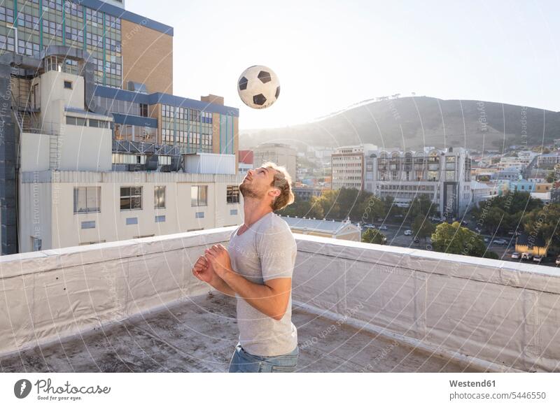 Junger Mann spielt Fussball auf der Dachterrasse Männer männlich Fußball Brüstung Balustrade üben ausüben Übung trainieren blond blonde Haare blondes Haar