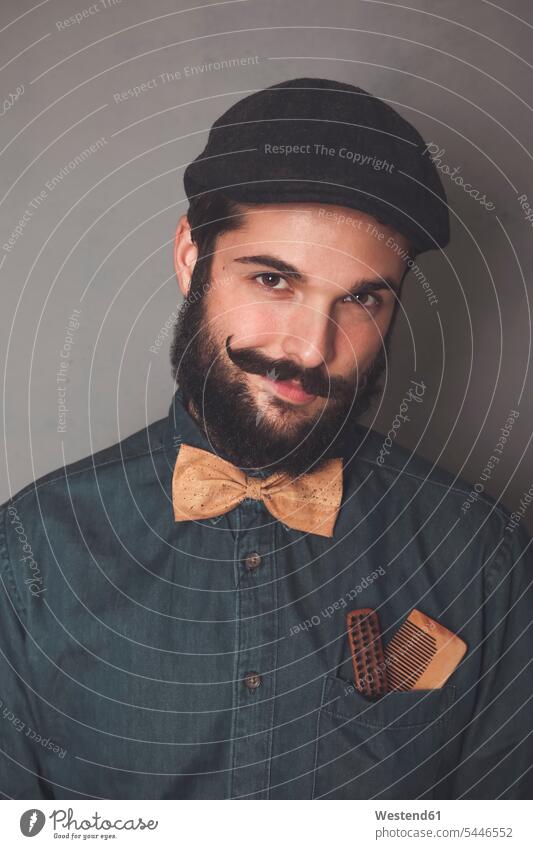 Bildnis eines bärtigen Mannes mit Mütze, Jeanshemd, Korkfliege, mit Holzkämmen als Bart und Schnurrbart in der Tasche Bärte Portrait Porträts Portraits Männer