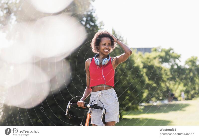Lächelnde sportliche junge Frau mit Fahrrad im Park trainieren lächeln Parkanlagen Parks weiblich Frauen Bikes Fahrräder Räder Rad Erwachsener erwachsen Mensch