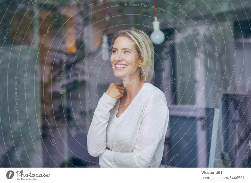 Porträt einer lachenden blonden Frau, die hinter einer Fensterscheibe steht Portrait Porträts Portraits weiblich Frauen Erwachsener erwachsen Mensch Menschen