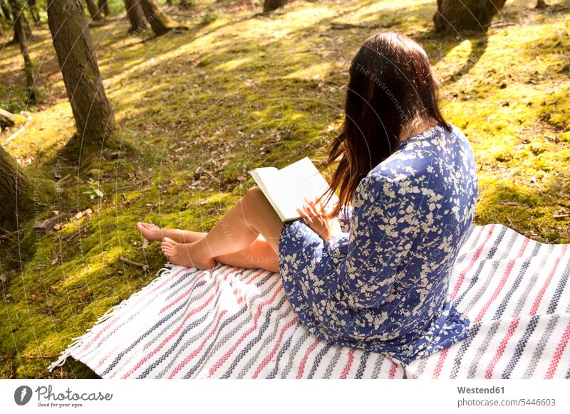Junge Frau sitzt auf einer Decke im Wald und liest ein Buch lesen Lektüre sitzen sitzend weiblich Frauen Forst Wälder Bücher entspannt entspanntheit relaxt