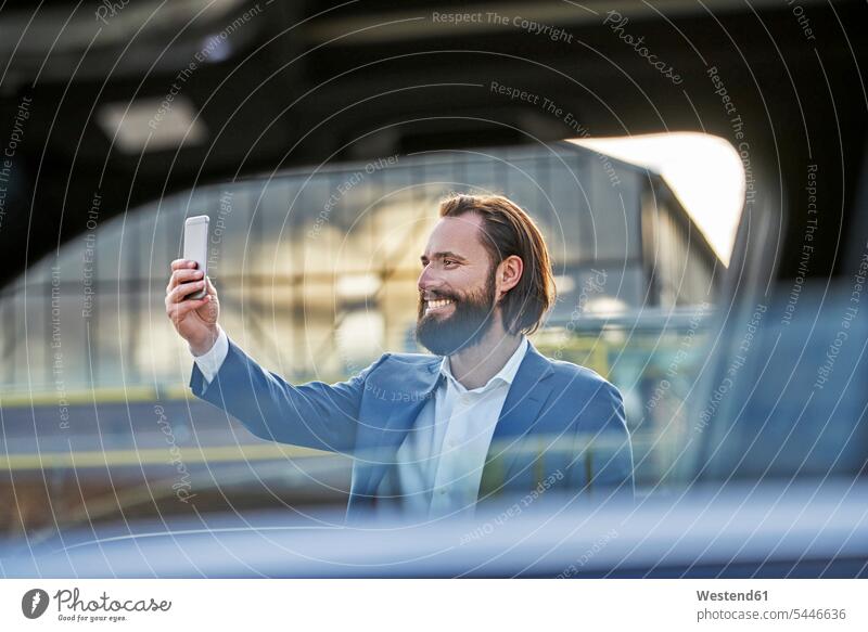 Lächelnder Geschäftsmann macht ein Selfie vor dem Auto Handy Mobiltelefon Handies Handys Mobiltelefone Selfies lächeln Businessmann Businessmänner
